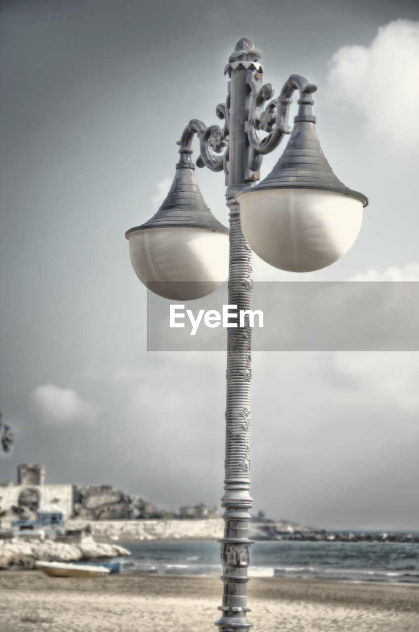 Low angle view of street light by sea against sky