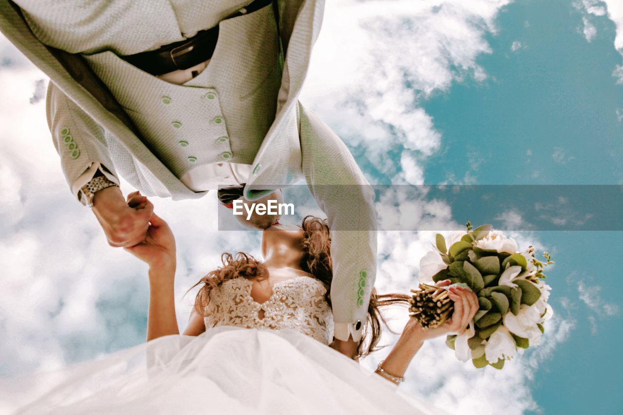 LOW SECTION OF WOMEN WITH ARMS OUTSTRETCHED AGAINST CLOUDY SKY