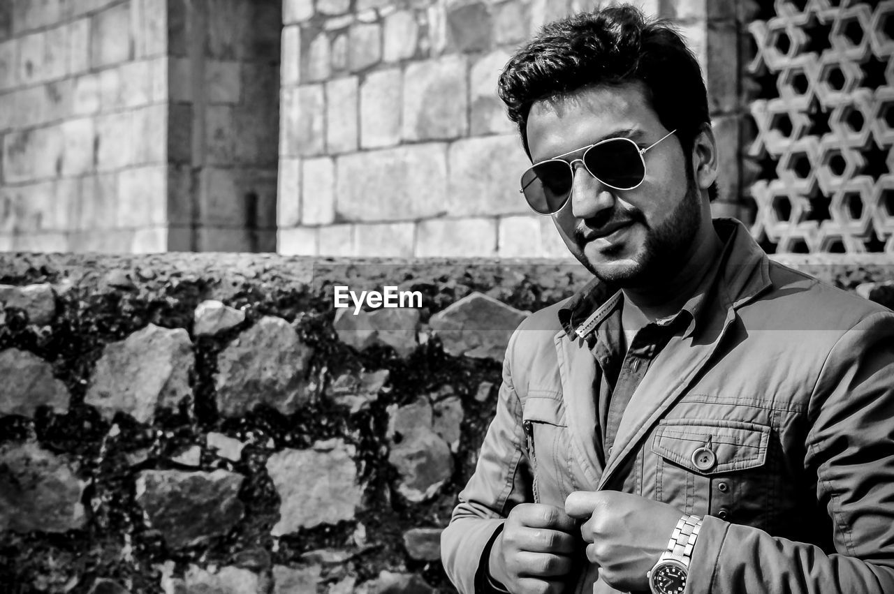 Portrait of young man wearing sunglasses standing against wall