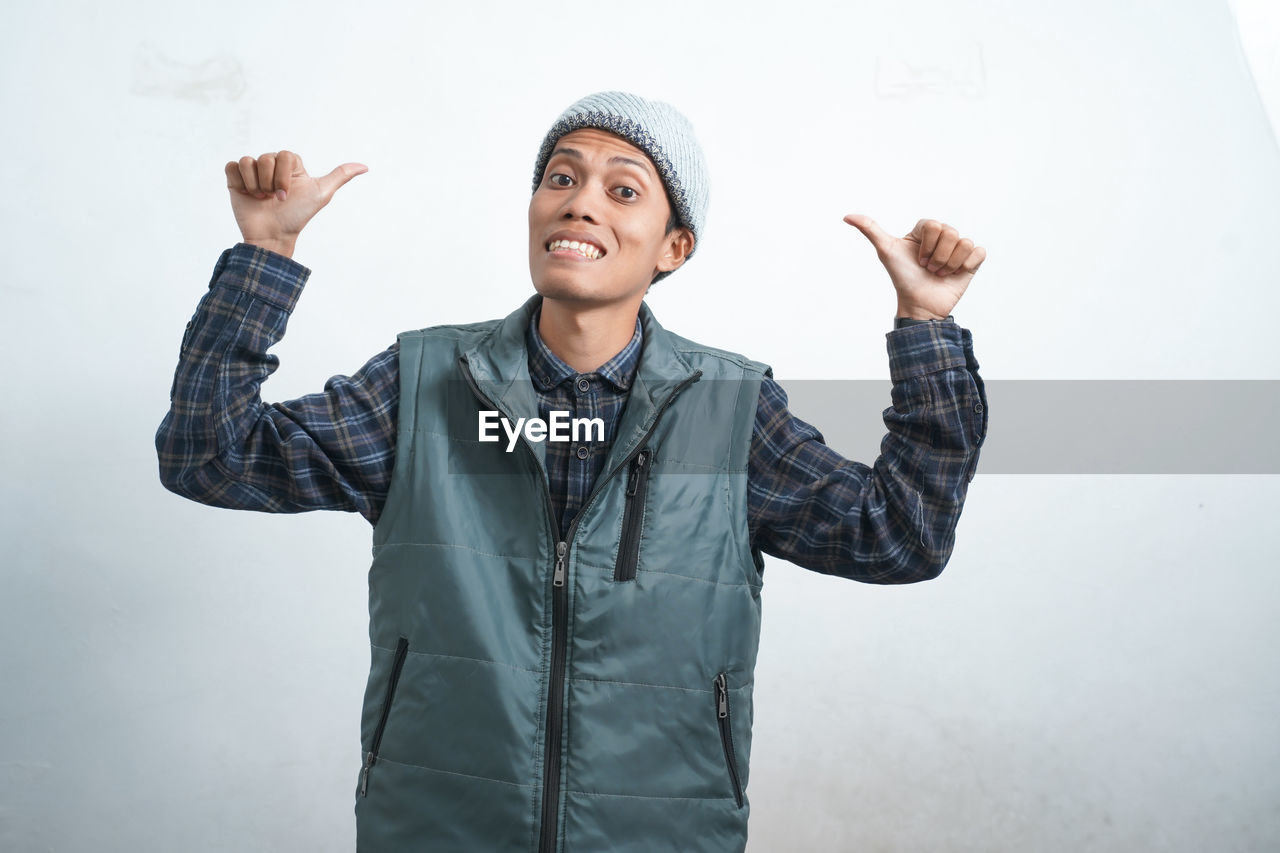 one person, adult, arm, waist up, standing, arms raised, clothing, gesturing, happiness, person, emotion, smiling, indoors, front view, hand raised, hand, business, men, limb, jacket, portrait, looking, copy space, human limb, cheerful, studio shot, occupation, casual clothing, positive emotion, gray, sign language, human face, young adult, looking up, mature adult