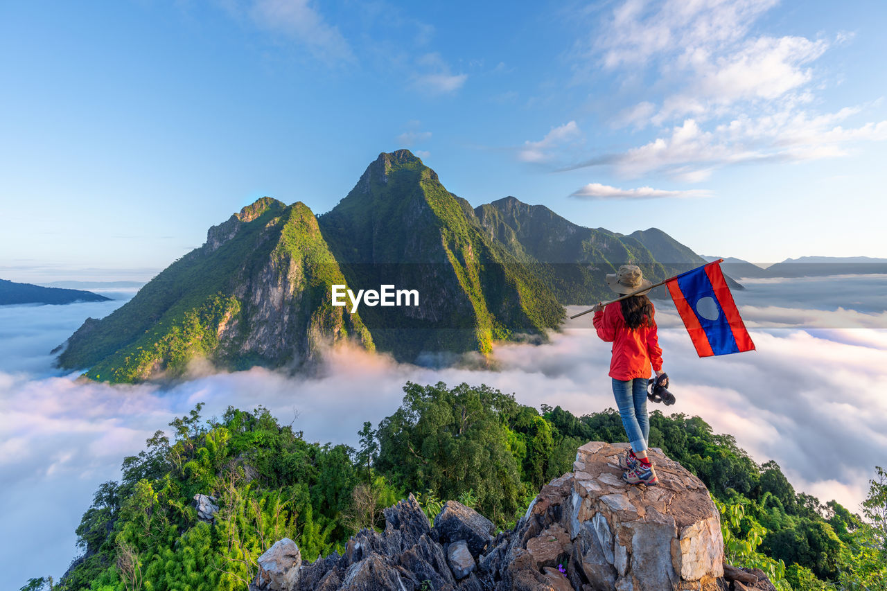 Asian girl holding laos flag on top of viewpoint of nong khiaw - a secret village in laos. 