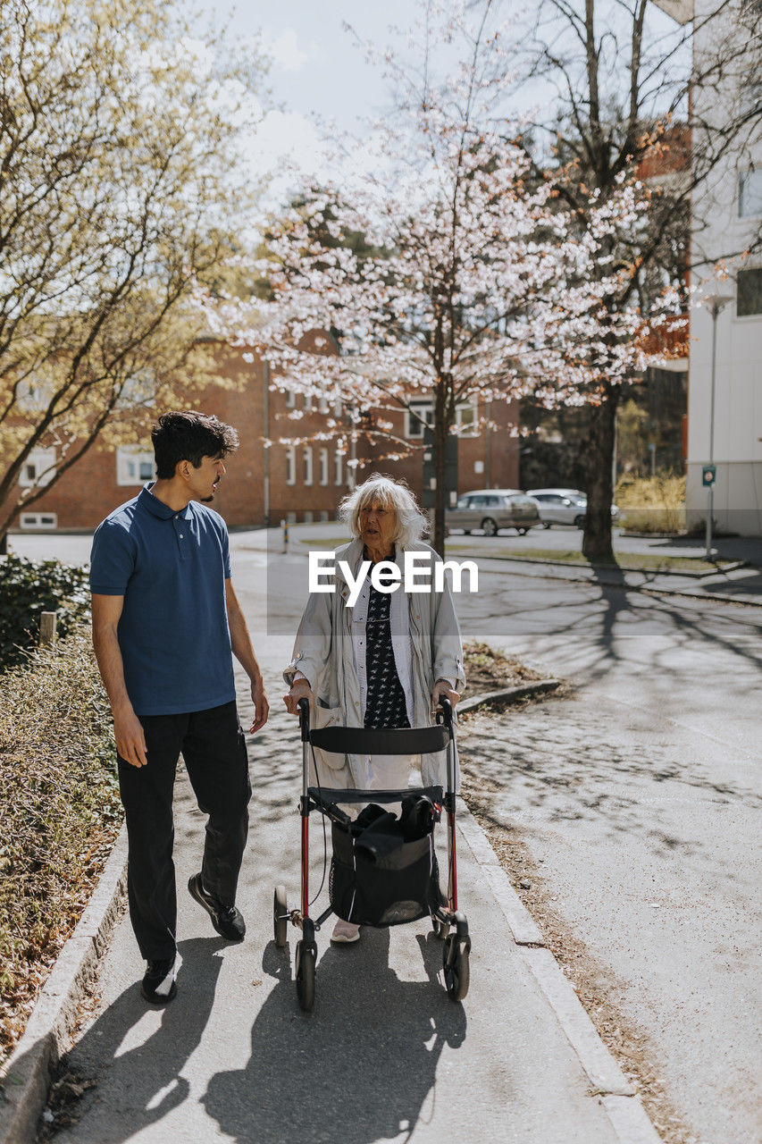 Male caregiver walking with senior woman using walker on sidewalk