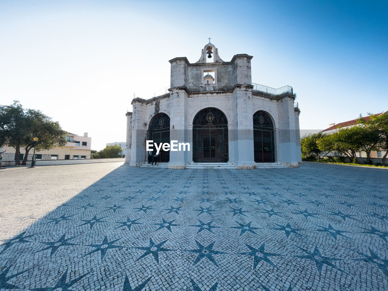 Octagonal backlit church casts long shadow on star decorated cobblestone square in lisbon