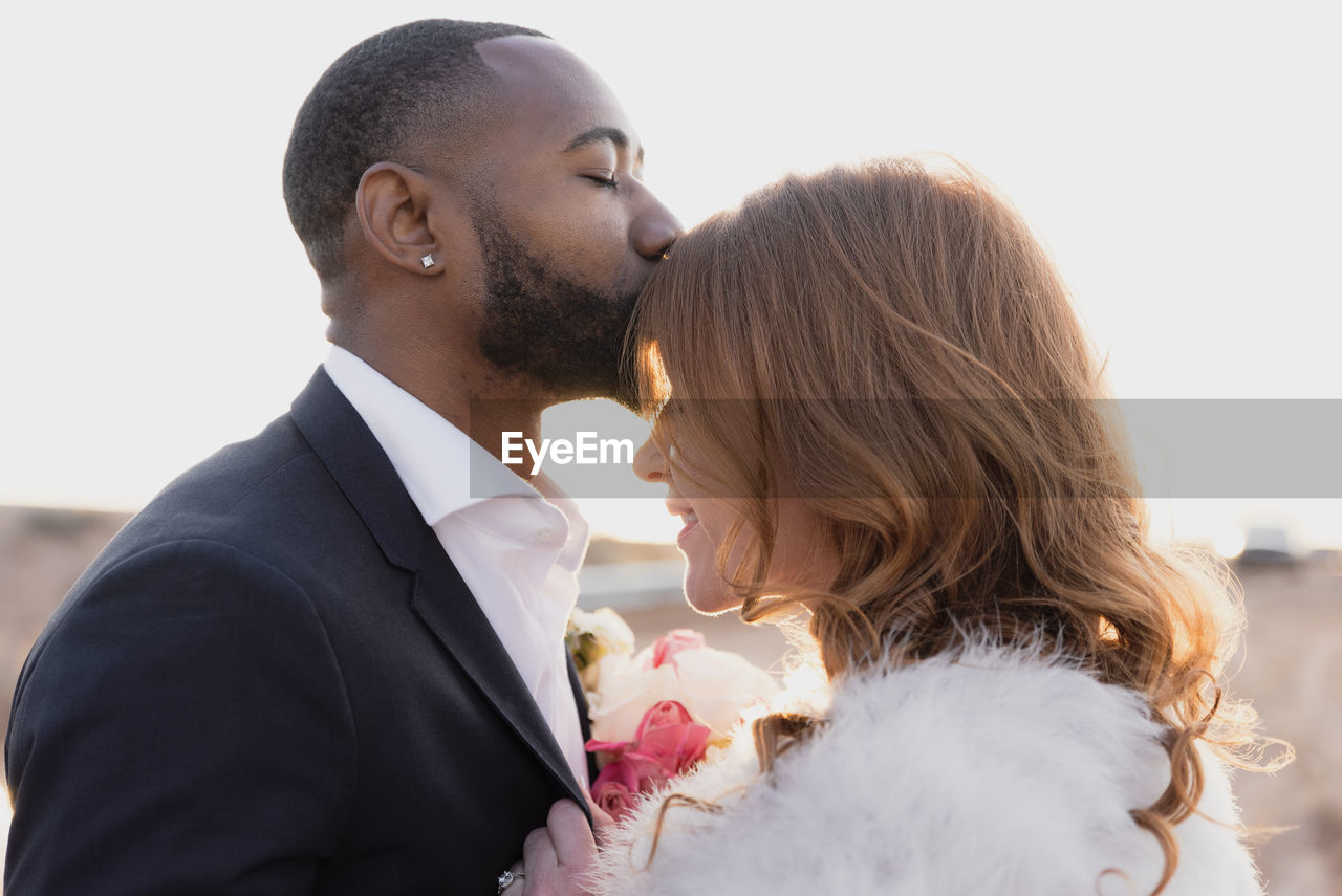 Side view of loving husband kissing on wife's forehead during sunset