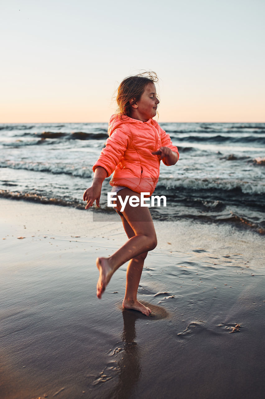 Playful little girl enjoying a free time over sea on a sand beach at sunset during summer vacation
