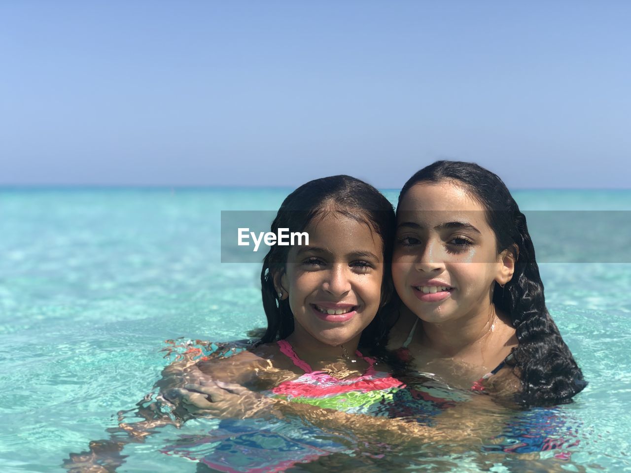 Two girls portrait in crystal clear water sea and clear blue sky