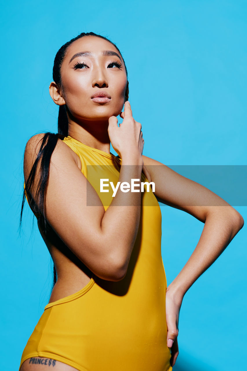 portrait of smiling young woman with eyes closed against blue background