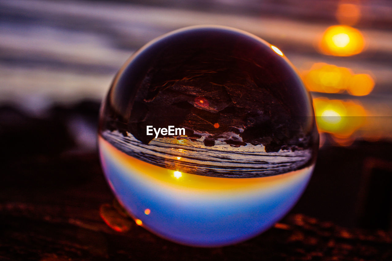 Close-up of crystal ball against sea during sunset