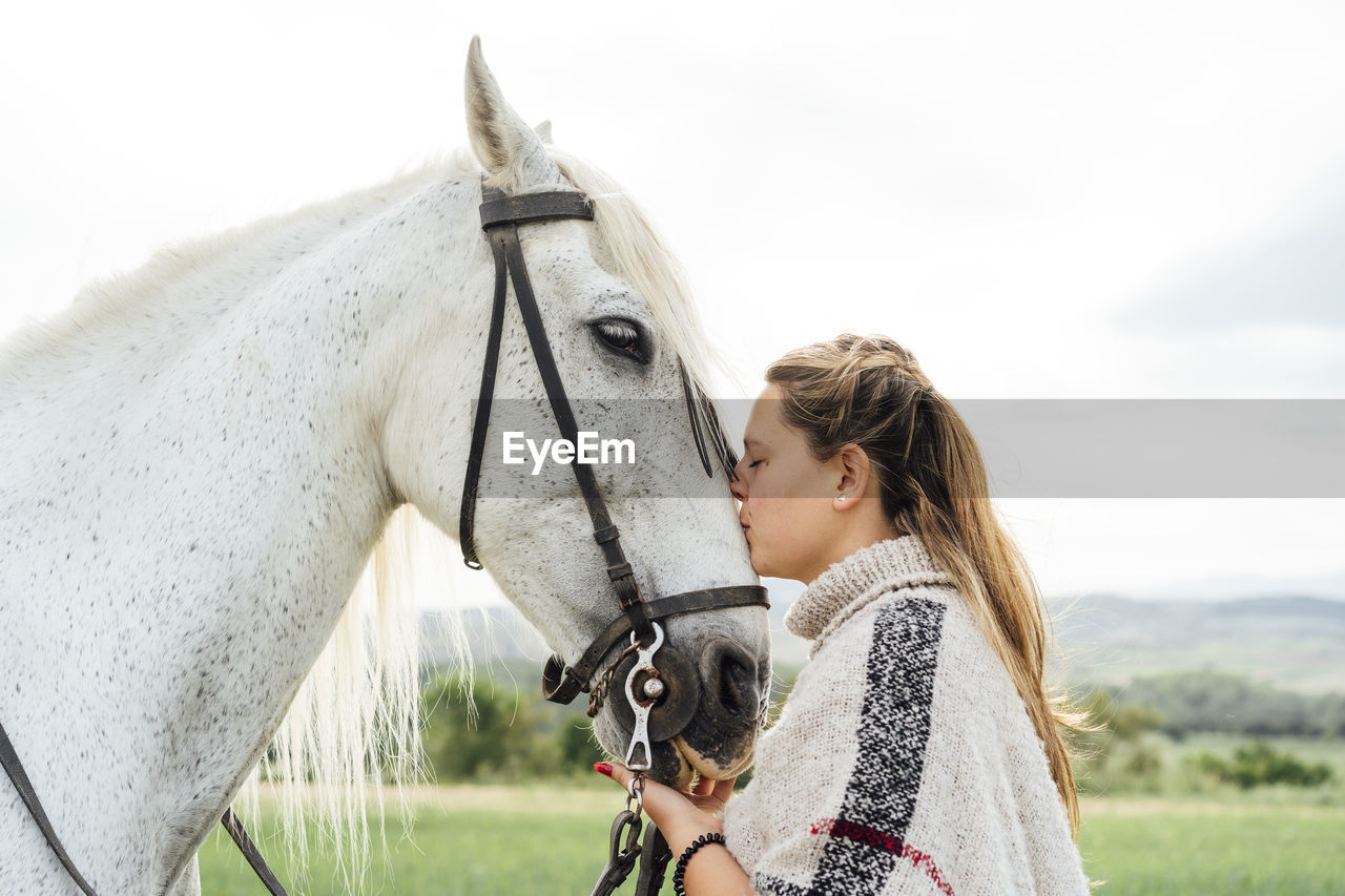 Young woman kissing white horse at countryside