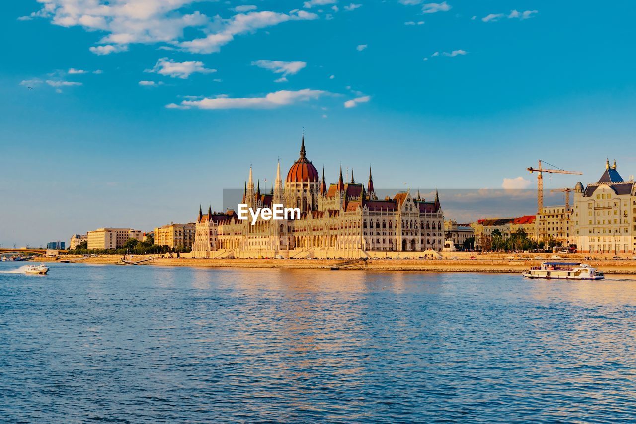 Hungarian parliament building by river against blue sky