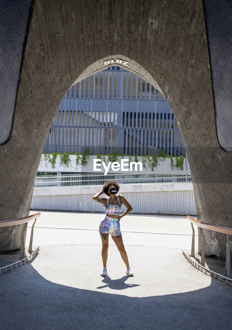 Confident african american female in medical mask and fashionable summer outfit standing in urban area in city during coronavirus outbreak