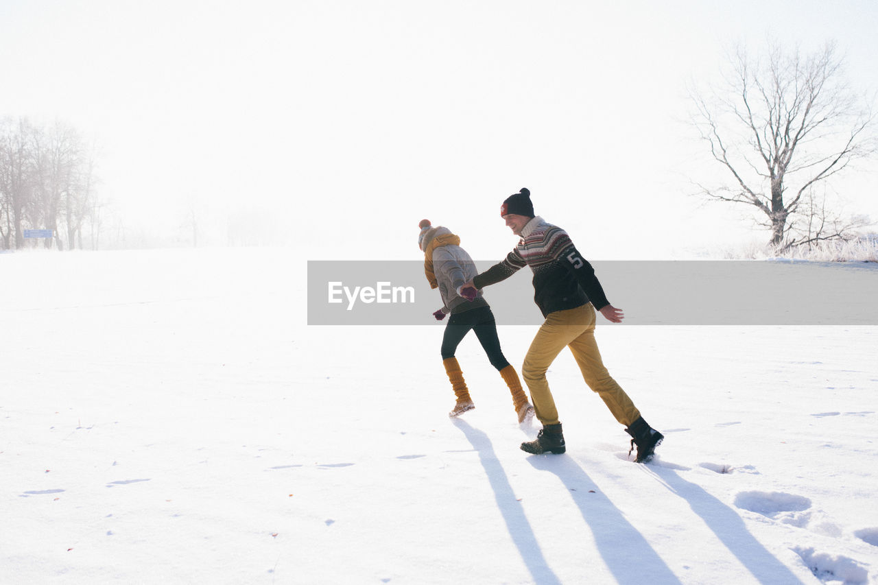 Couple running on snowy land against sky