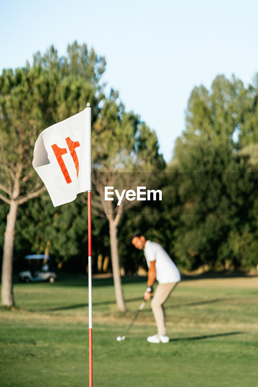 Attentive male athlete with putter and ball in golf field looking forward on summer day