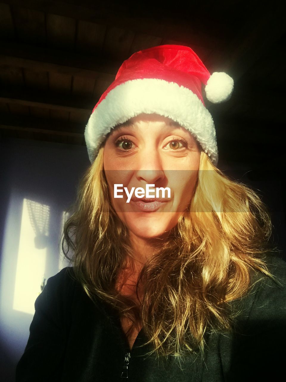 Low angle portrait of young woman with blond hair wearing santa hat at home