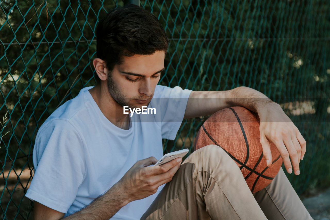 Boy looking at the phone with basketball ball outdoors