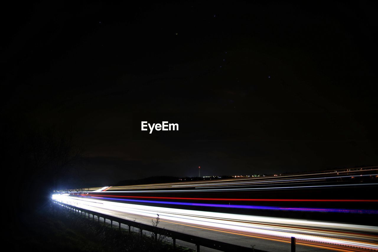 ILLUMINATED LIGHT TRAILS ON ROAD AGAINST SKY AT NIGHT