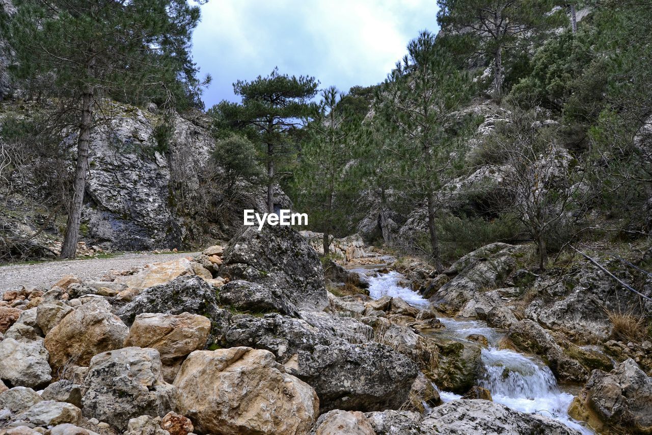 Stream flowing through rocks against cloudy sky