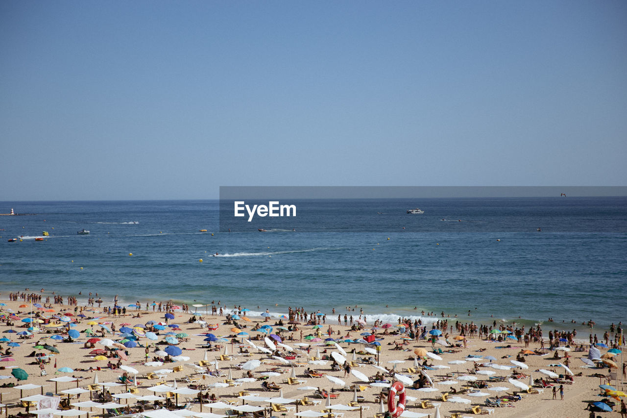 Scenic view of sea against clear sky of people on beach in portugal. 