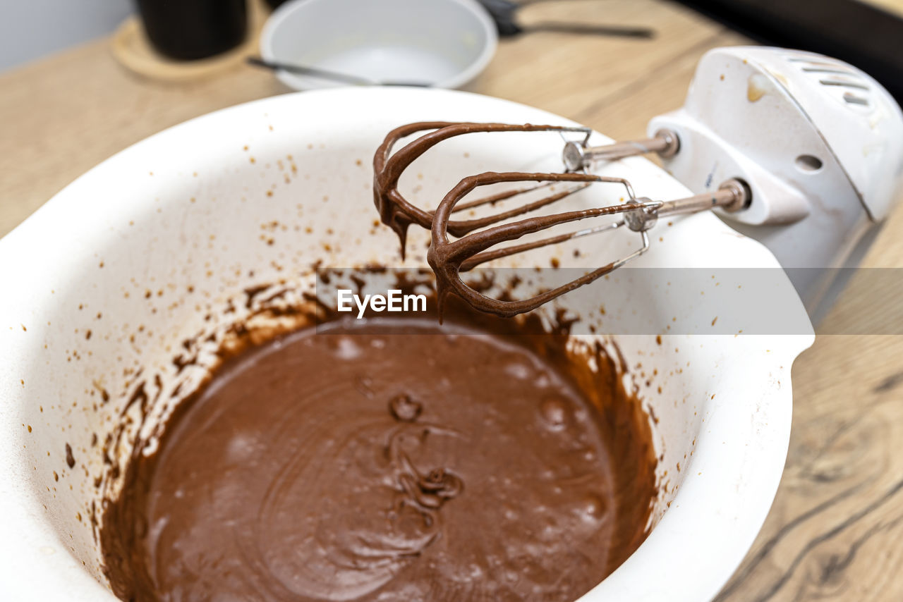 A standing hand mixer with a whisk next to the bowl, with raw dough, the dough  a thick brown state.