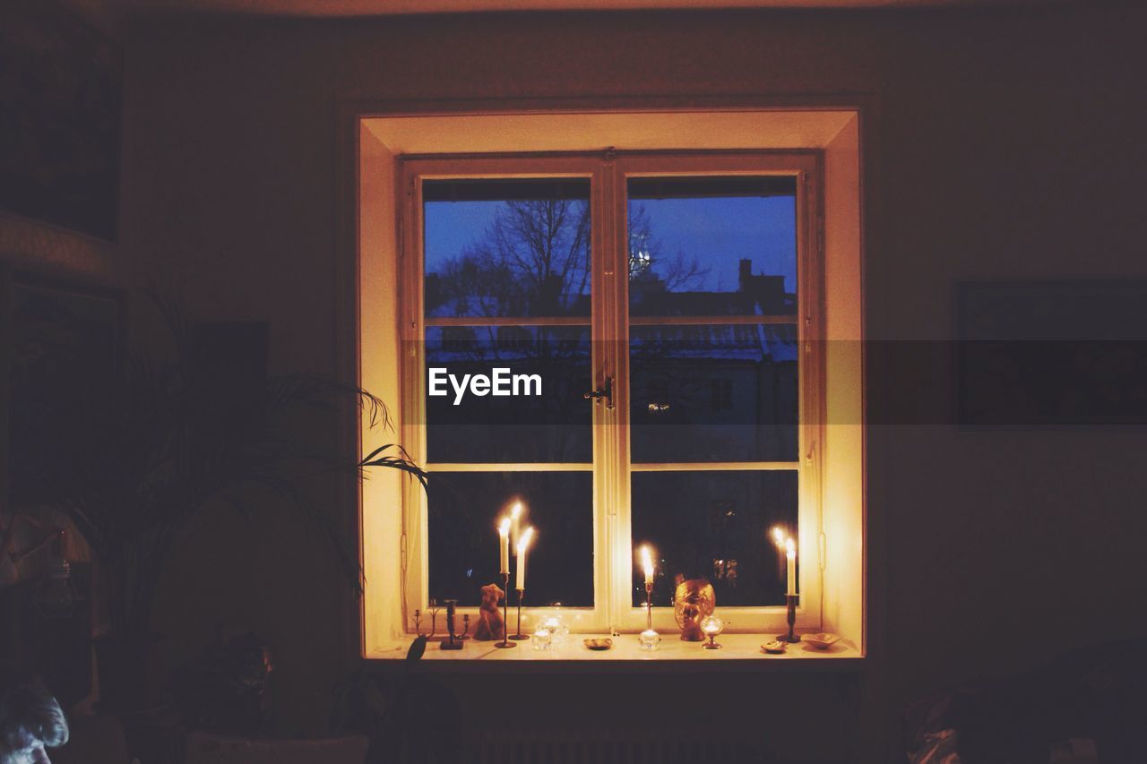 Burning candles on window sill at home