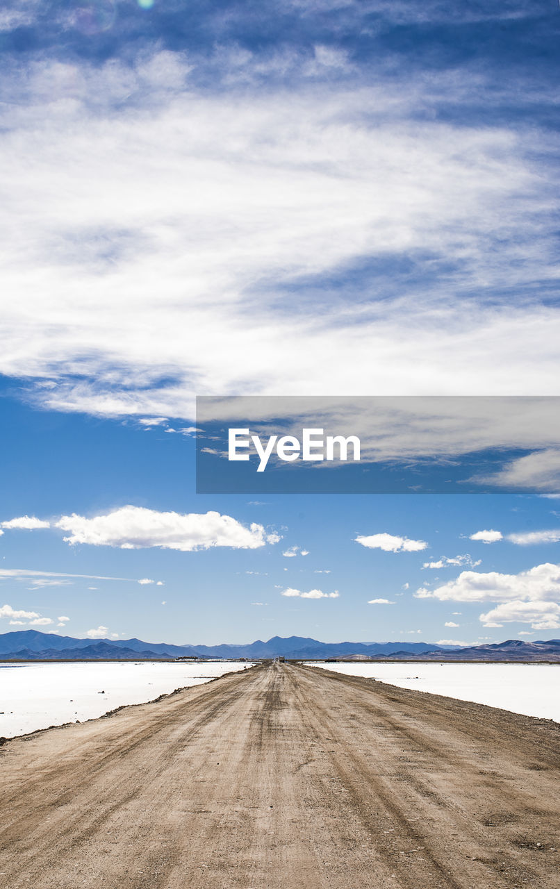 Empty road amidst snow covered landscape against cloudy sky