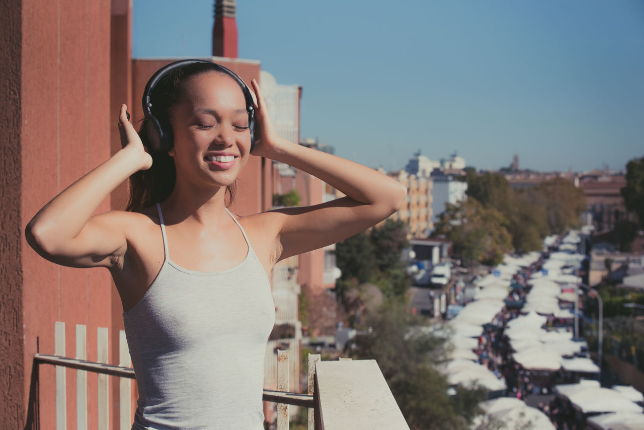 Close-up of woman listening music in city against sky