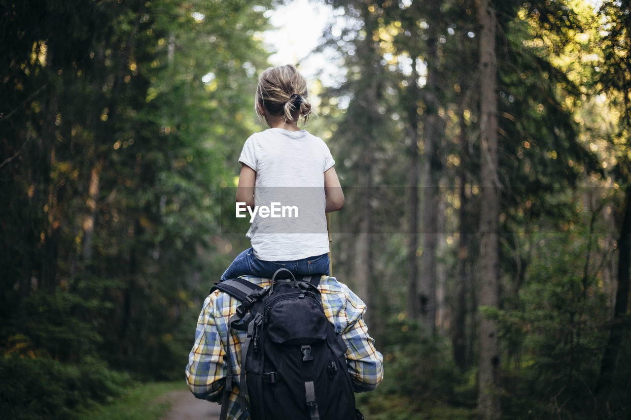 Rear view of father carrying daughter on shoulder while walking in forest