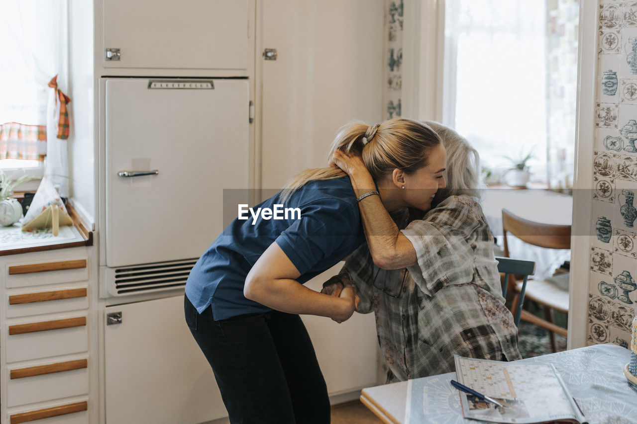 Senior woman embracing female care assistant at home