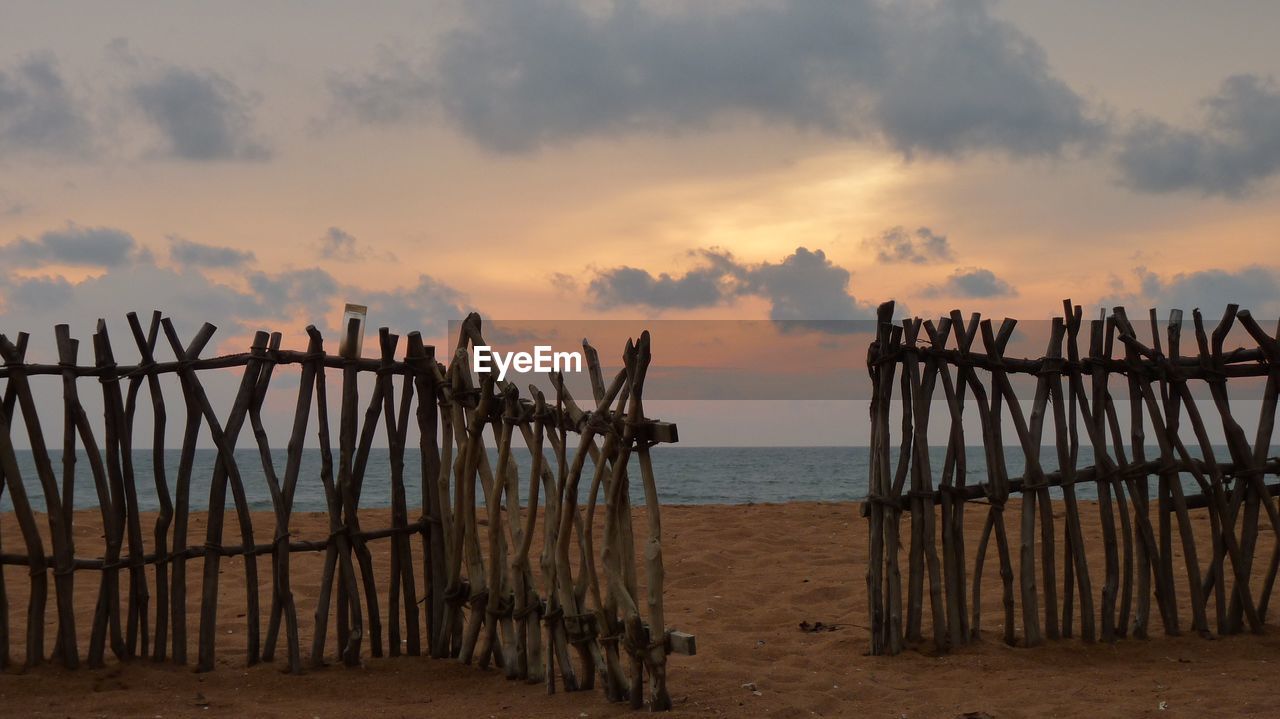 Wooden fence at beach against cloudy sky at dusk