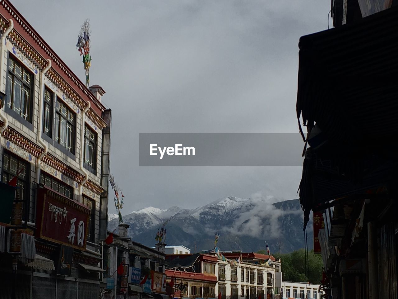 Low angle view of buildings in town by mountains against cloudy sky