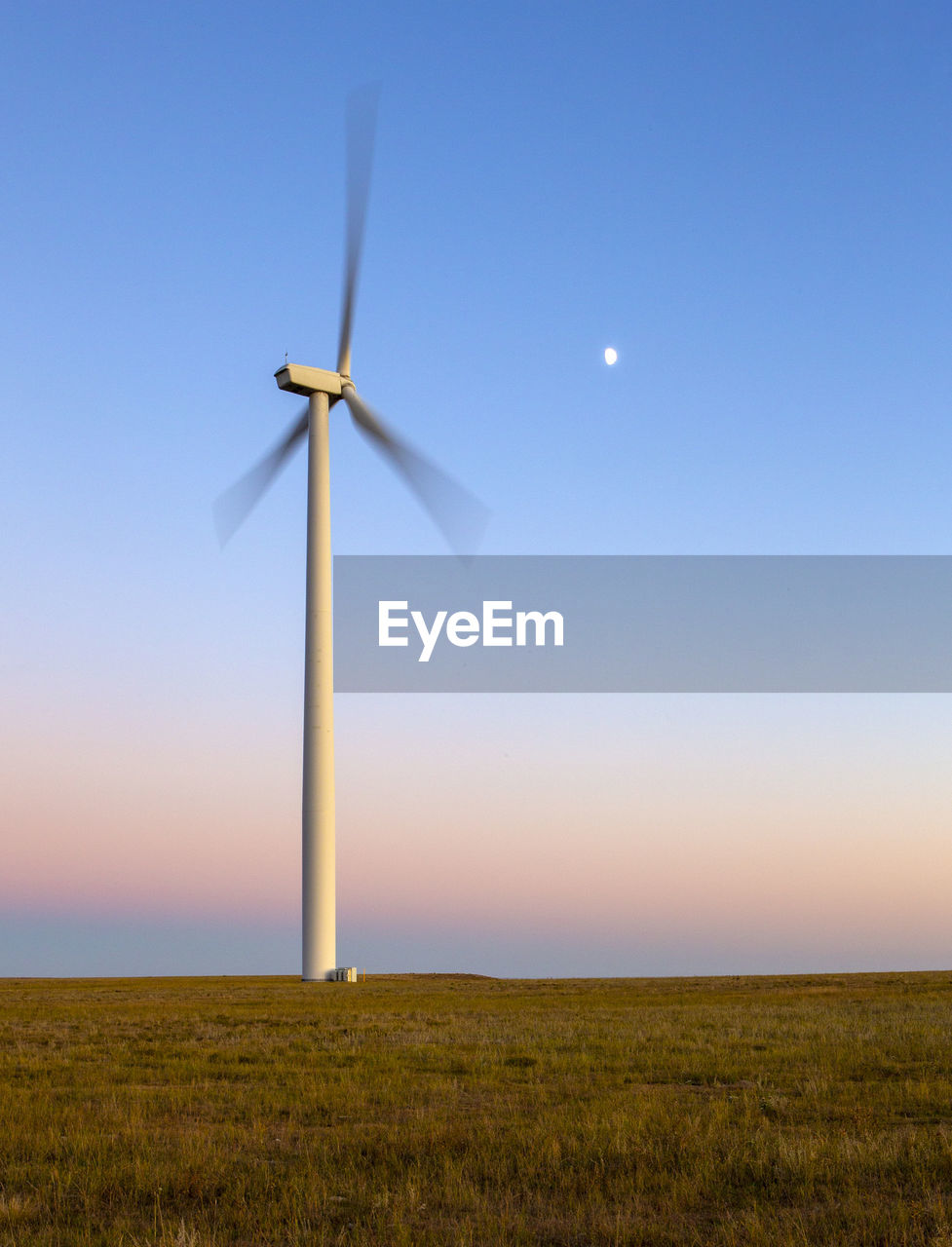 Wind turbine in motion against blue sky with moon