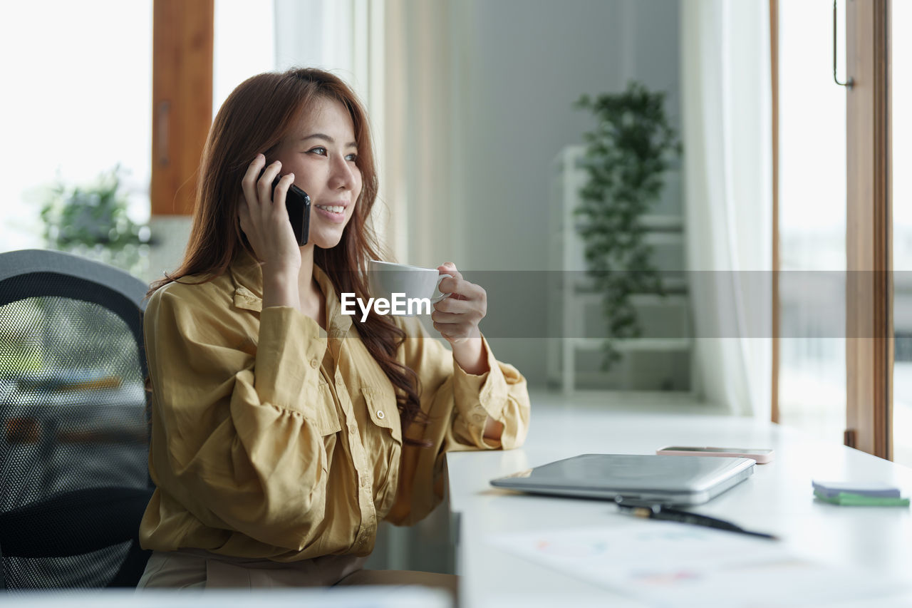 young woman using mobile phone while sitting at office