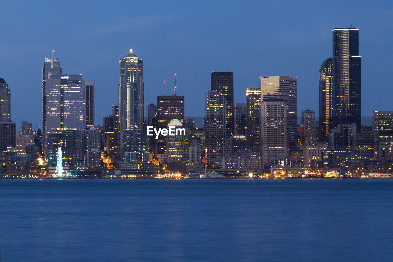 Illuminated buildings by sea against sky