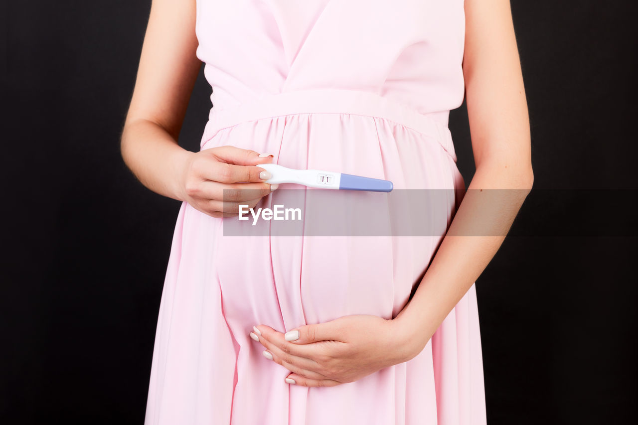 MIDSECTION OF WOMAN STANDING AGAINST PINK BACKGROUND