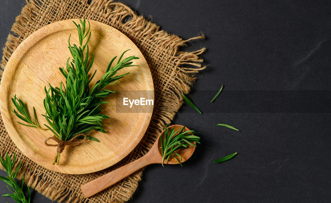 Top view of branch fresh rosemary in wood plate on black background. 