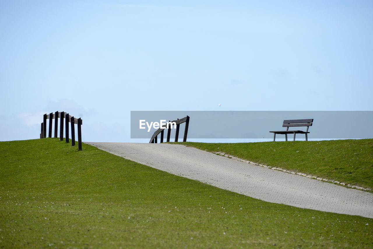 Empty park bench on field against sky