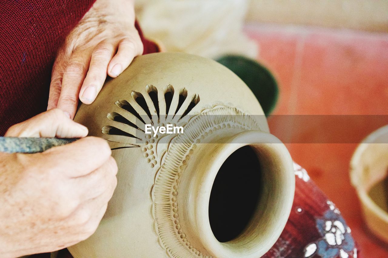 Close-up of person hands carving on earthenware
