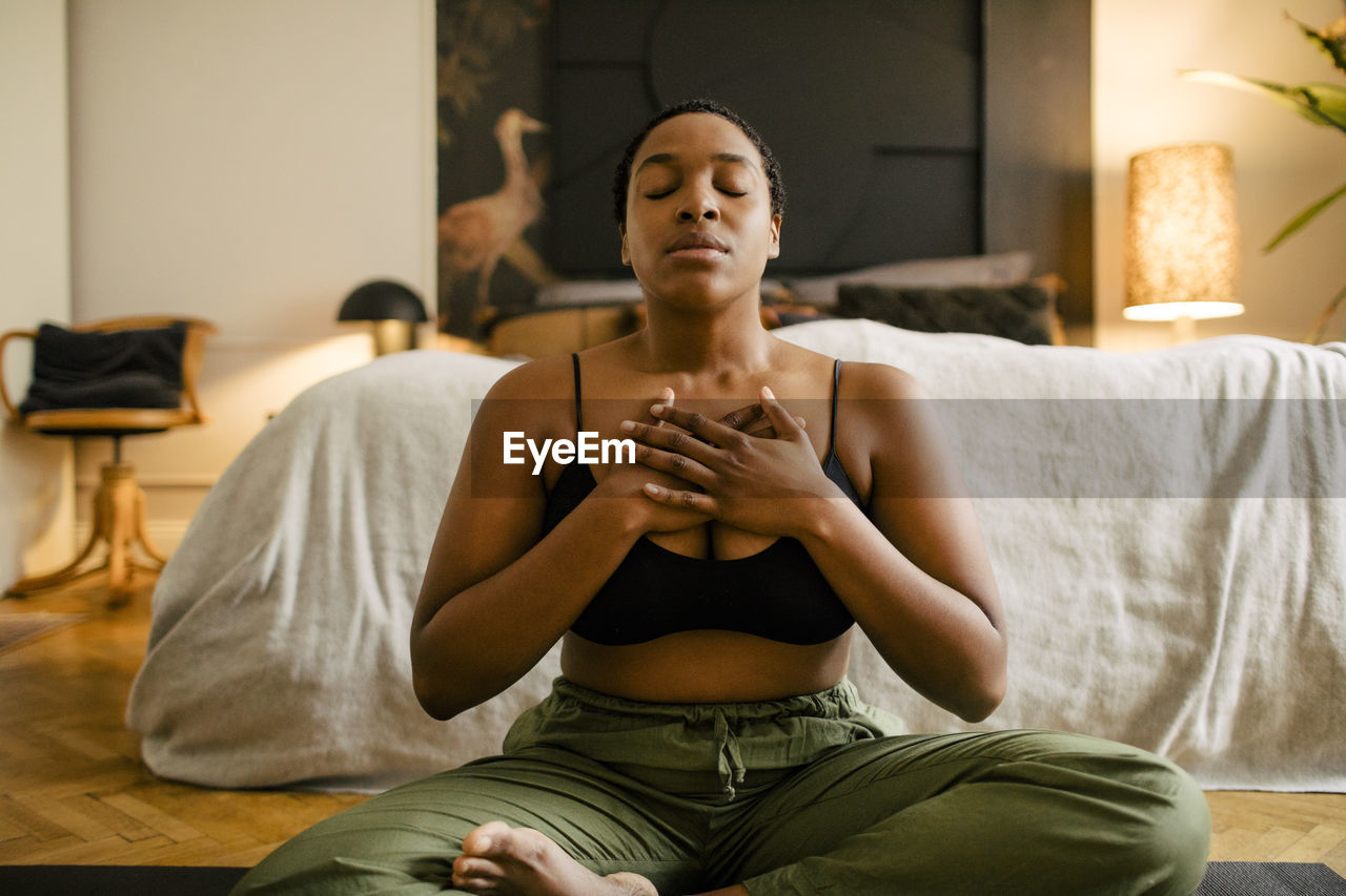 Woman meditating on exercise mat in bedroom at home