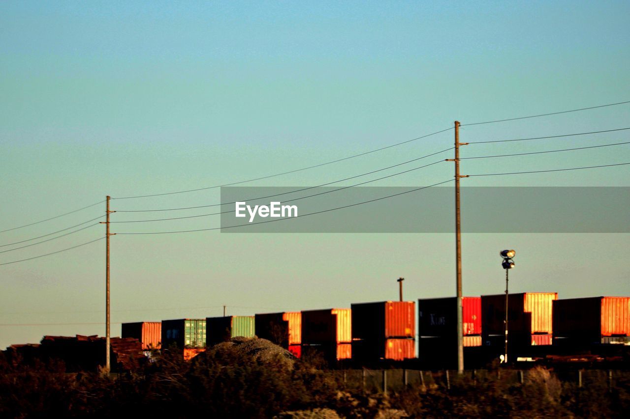 Low angle view of electricity pylons by cargo containers