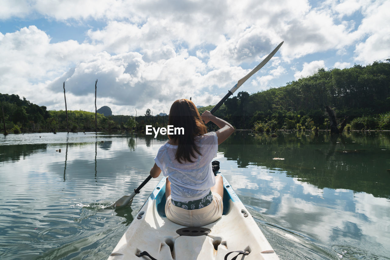 REAR VIEW OF WOMAN ON LAKE BY TREES AGAINST SKY