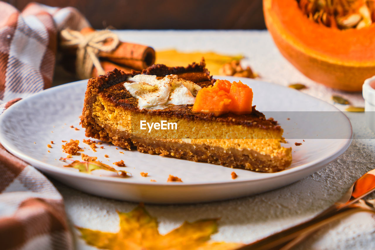 Homemade pumpkin cheesecake decorated with whipped cream on gray plate.