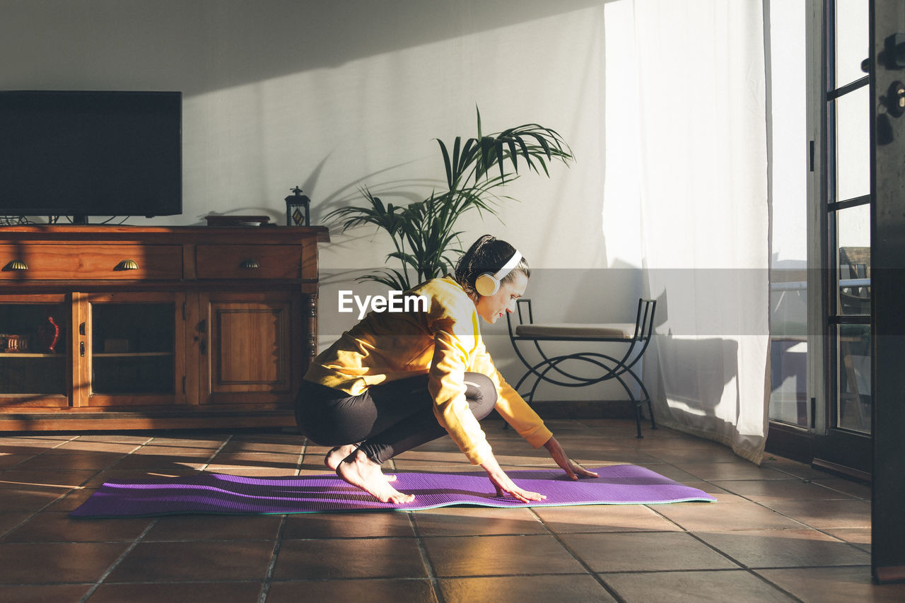 Young caucasian brunette woman listening music to practice yoga at home.