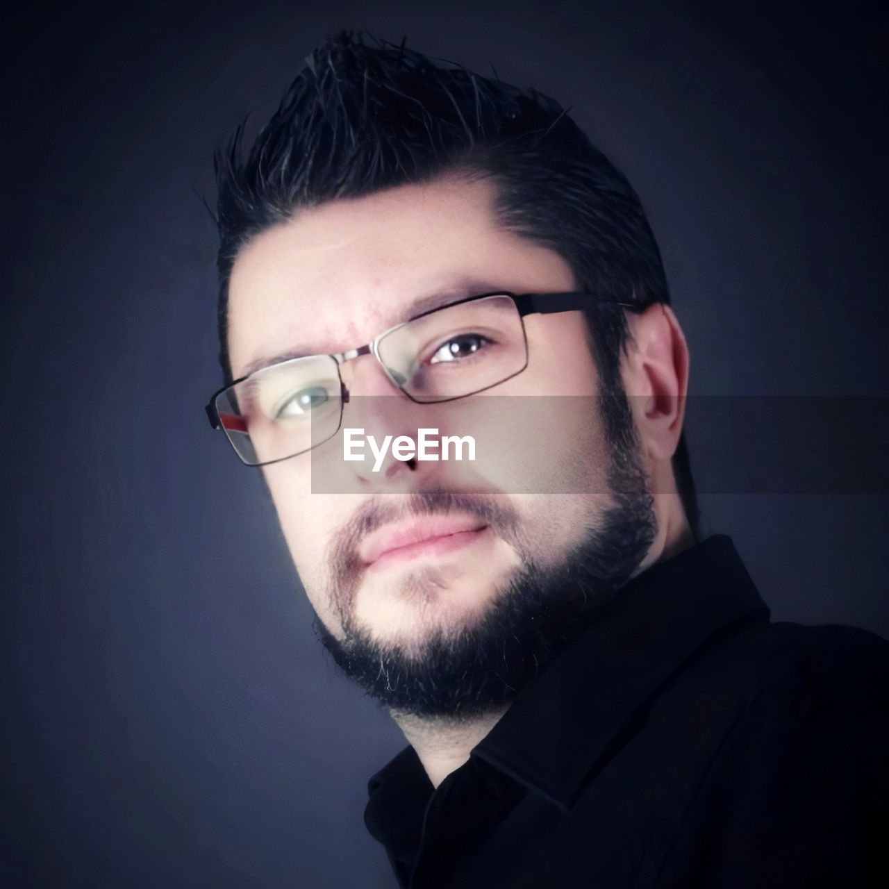 PORTRAIT OF YOUNG MAN WITH EYEGLASSES AGAINST BLACK BACKGROUND