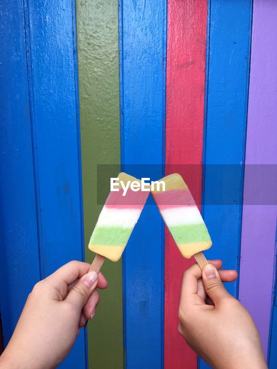 Close-up of people holding popsicle against multi colored wall