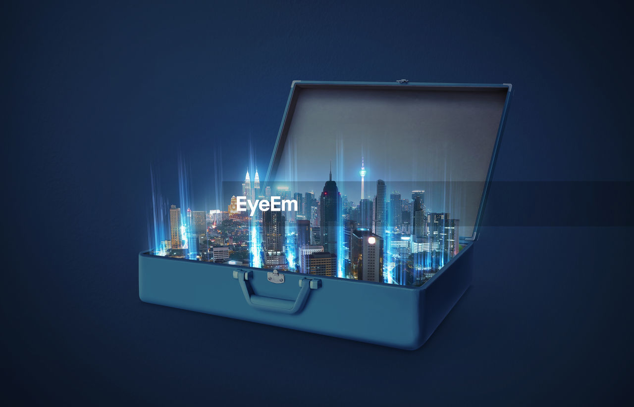 Digital composite image of illuminated modern cityscape in luggage over blue background