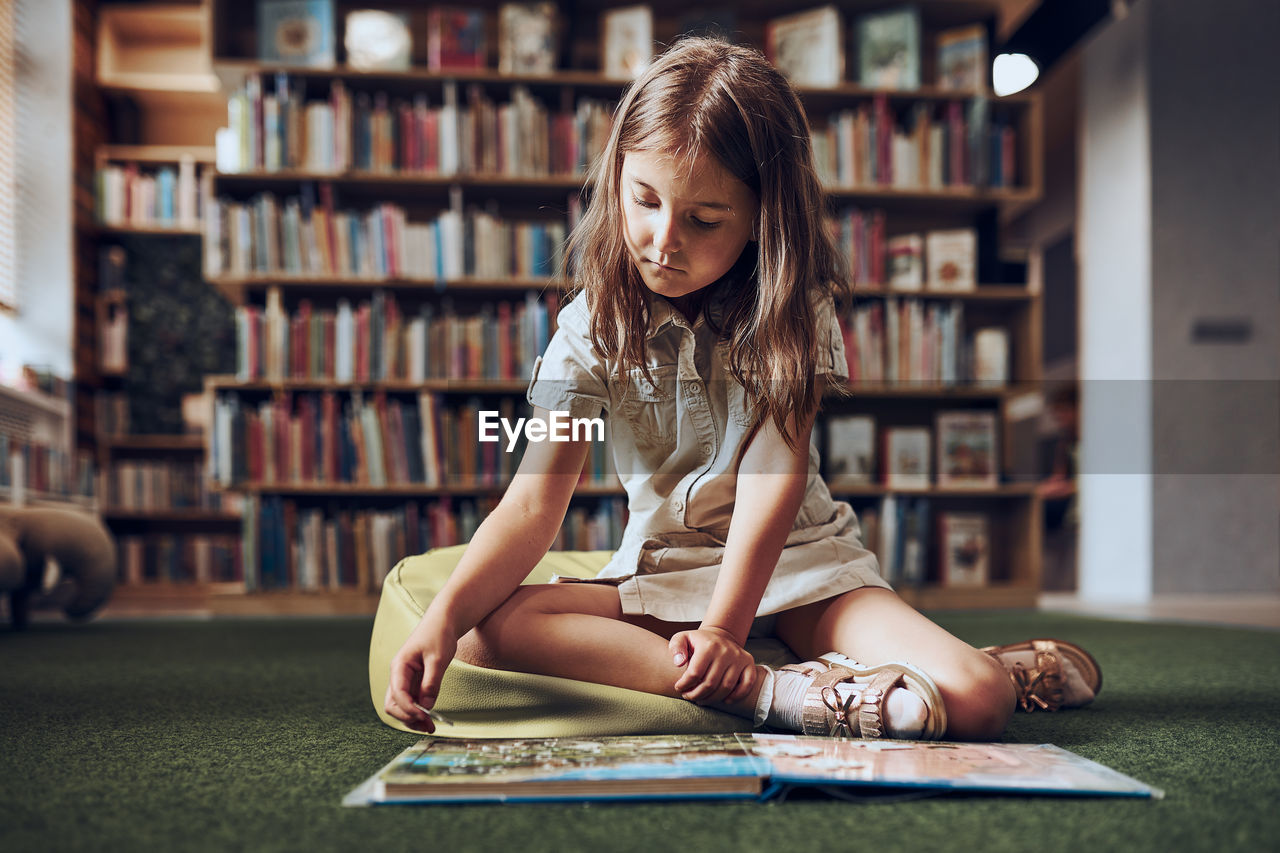 Child solving riddle in book in school library. primary school girl is involved in book with riddles