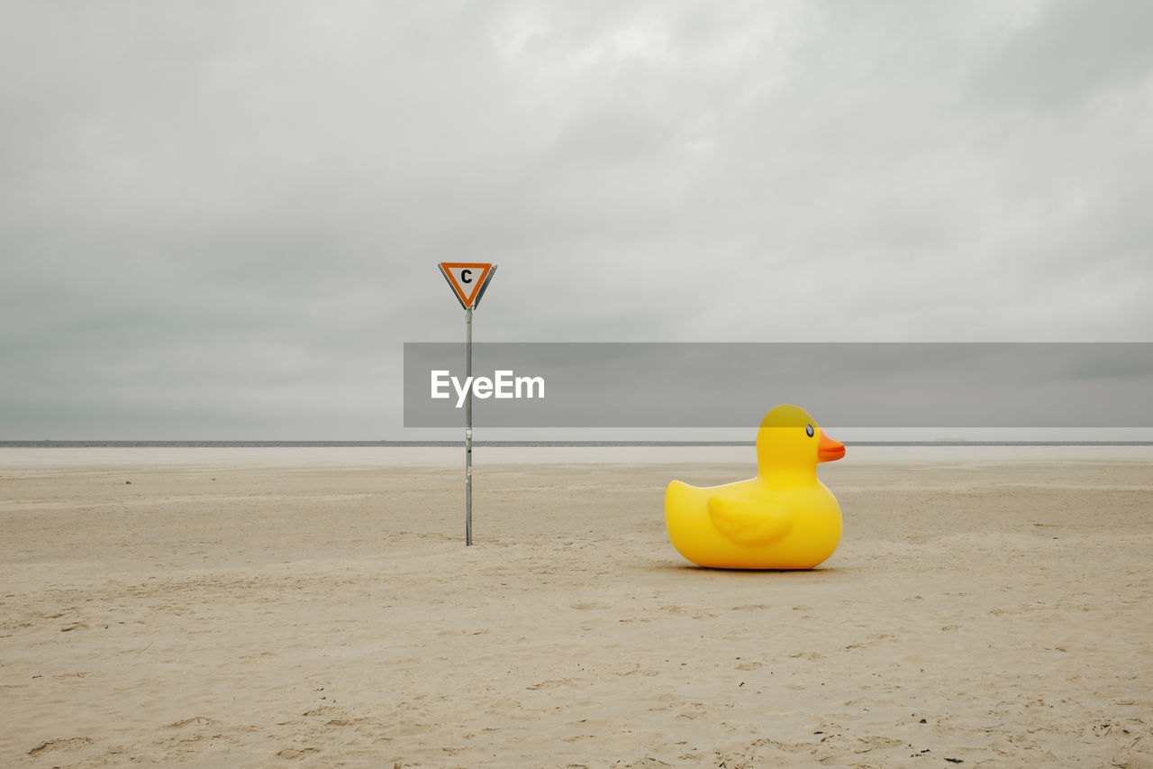 Rubber duck on a beach near sign