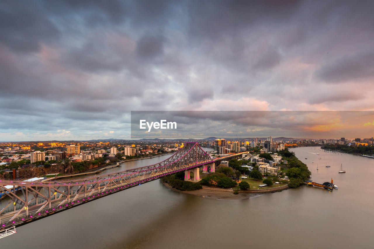 Bridge over river in city against cloudy sky