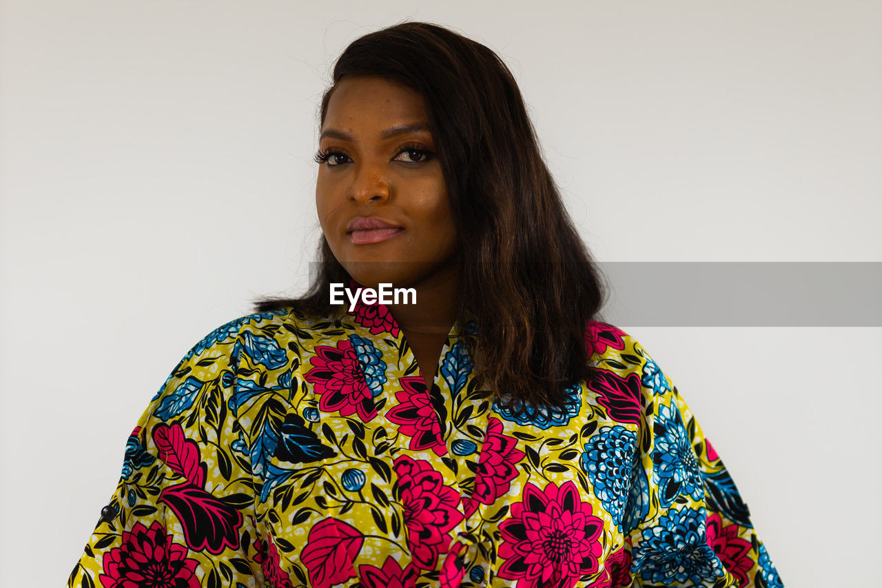 portrait, one person, studio shot, adult, indoors, women, looking at camera, hairstyle, photo shoot, young adult, white background, clothing, copy space, front view, sleeve, waist up, headshot, black hair, long hair, emotion, gray background, person, serious, pattern, smiling, individuality, standing, multi colored, fashion, female, floral pattern, cut out, looking, brown hair