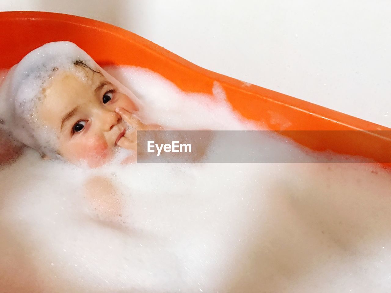 Portrait of smiling baby covered with soap sud in bathtub by wall